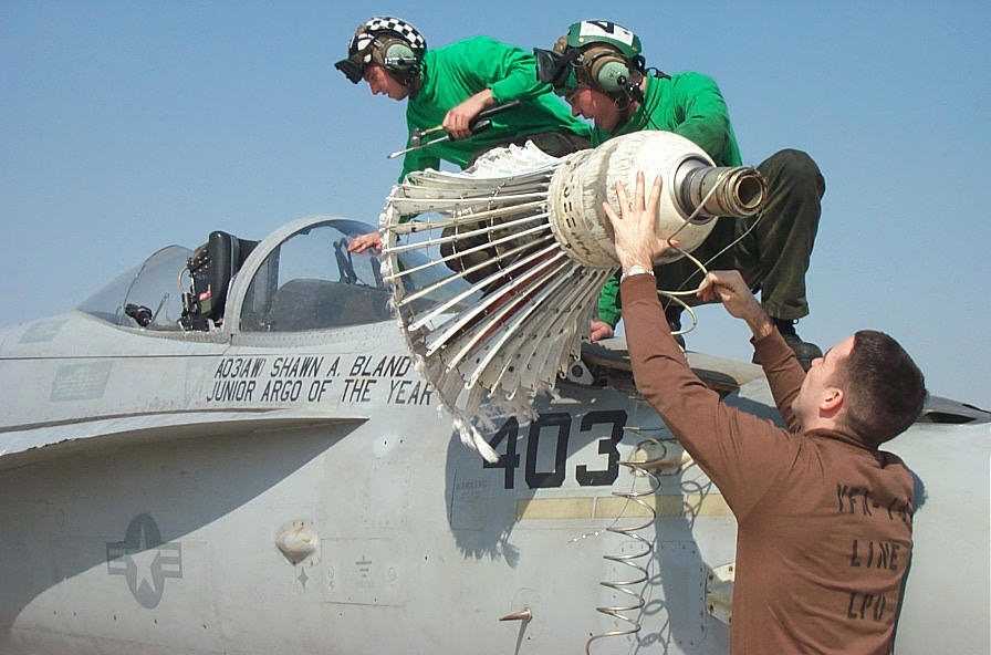 Two flight-deck crewmen and a maintainer working the snagged refueling basket and hose off the nose of F/A-18 403.