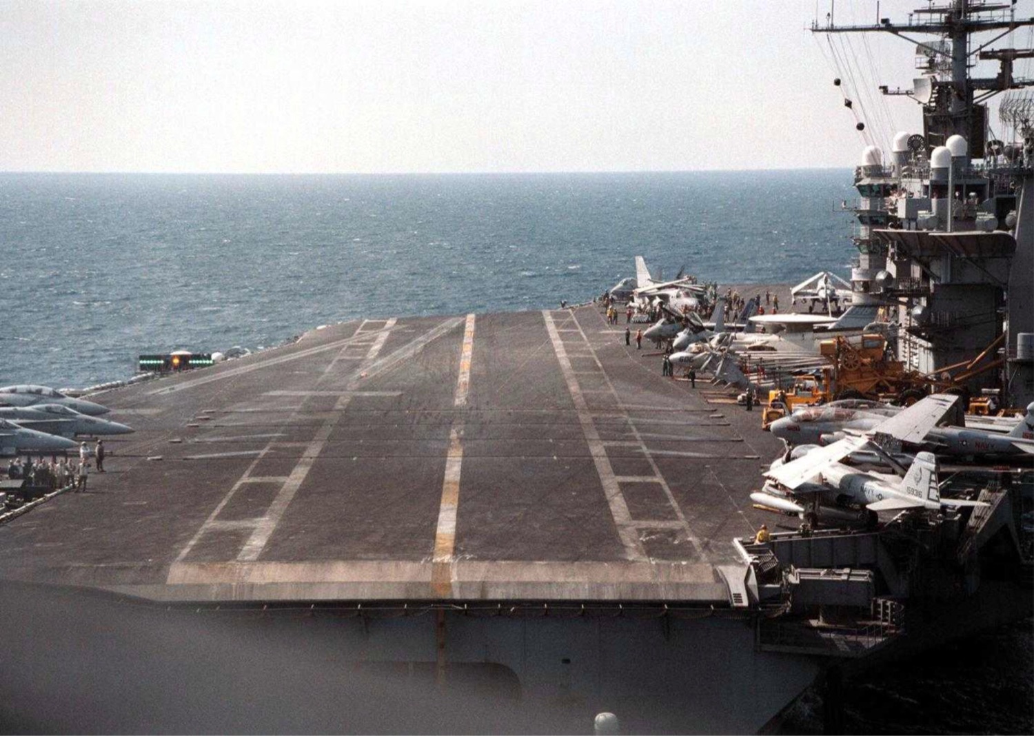 The angled flight deck of an aircraft carrier, aircraft parked along the edge, open sea beyond.