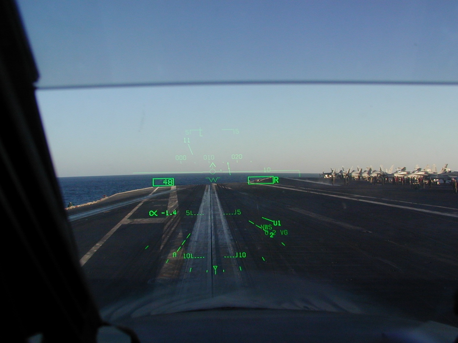 Cockpit view through the HUD on final approach to the carrier deck, green symbology over the landing area.